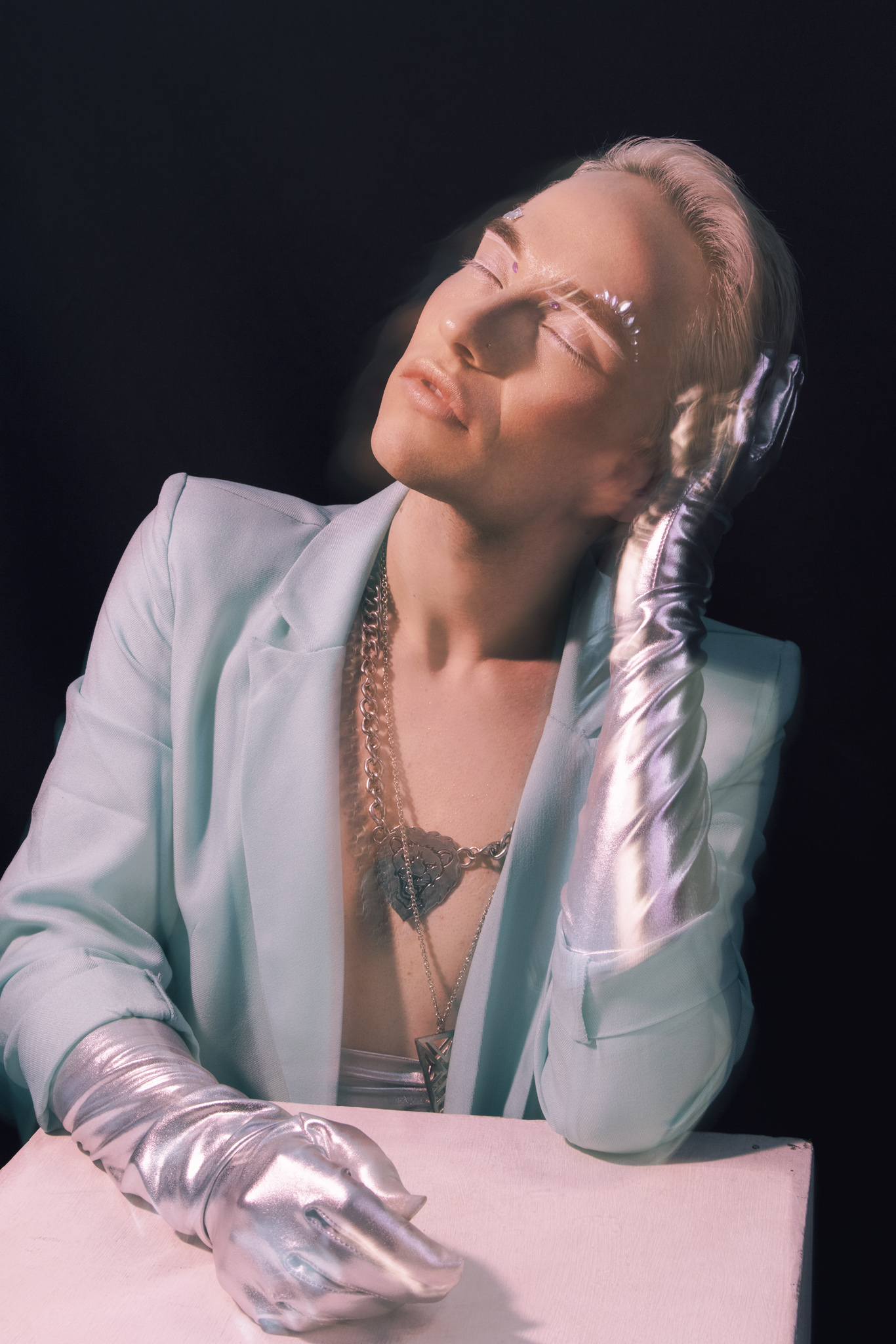 Charlie Void in ice-blue tailoring beneath a narrow beam of light